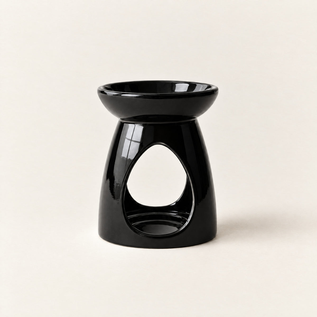 Ceramic wax melt burner in glossy black, with a teardrop opening for a tea-light, on a plain ivory background