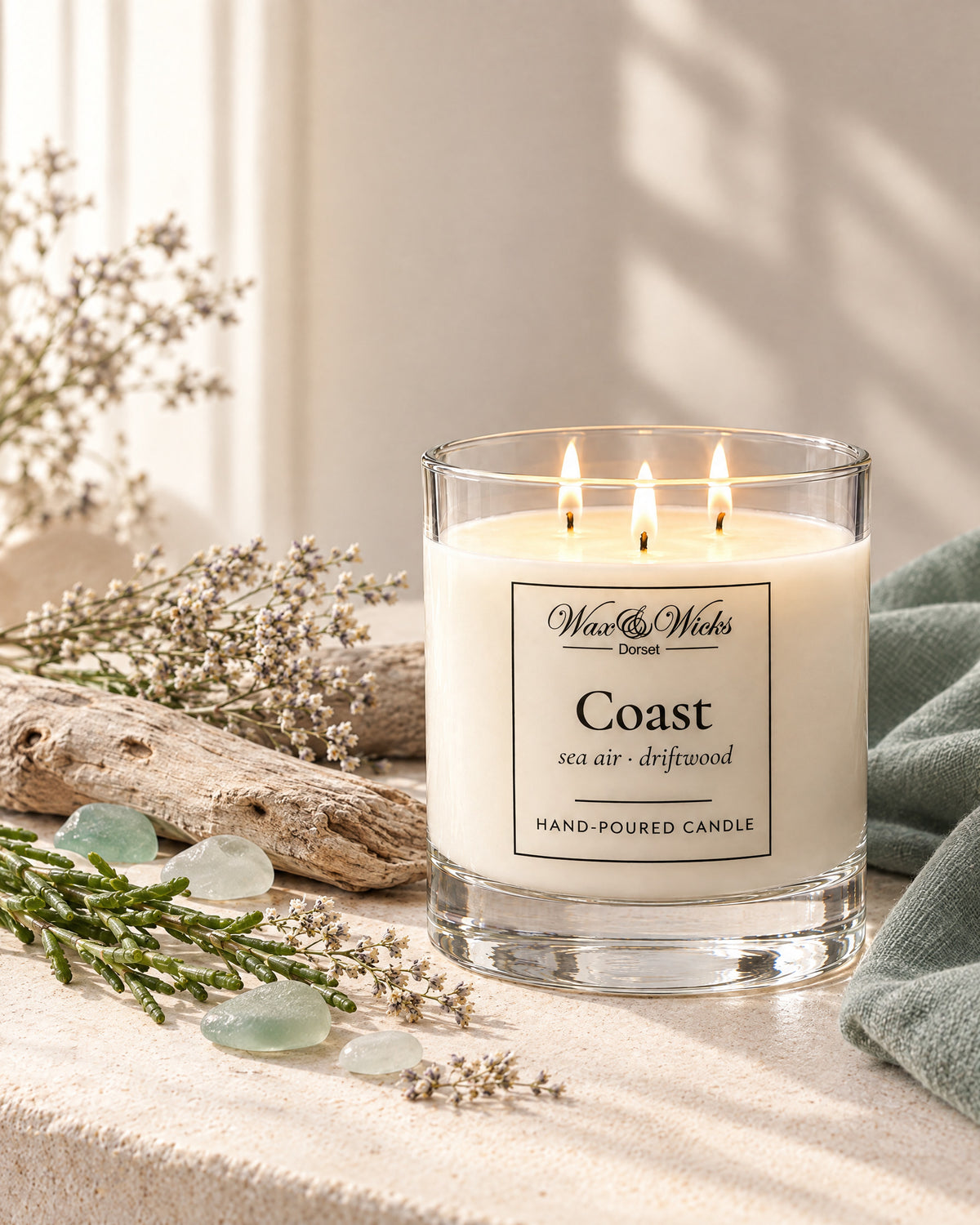 Large Coast candle, three wicks, in a clear glass jar, styled with bleached driftwood, sea-glass pebbles, dried sea lavender and samphire