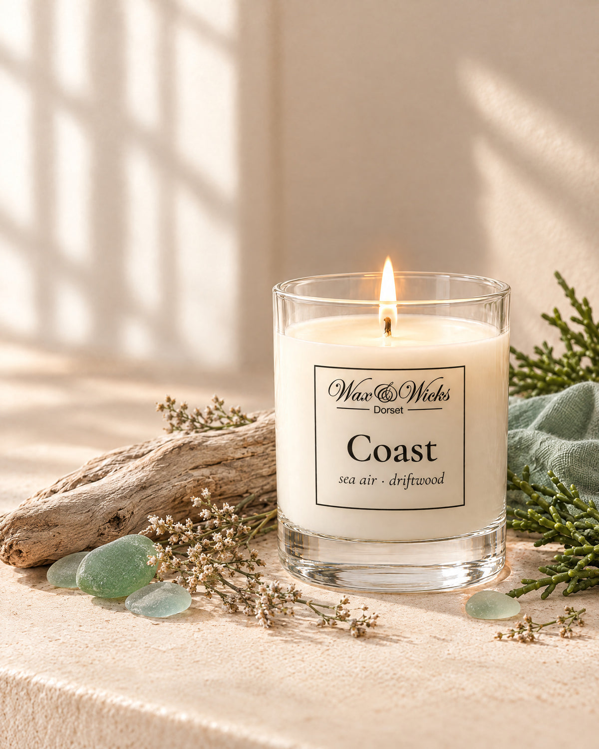 Small Coast candle, one wick, in a clear glass jar, styled with bleached driftwood, sea-glass pebbles, dried sea lavender and samphire