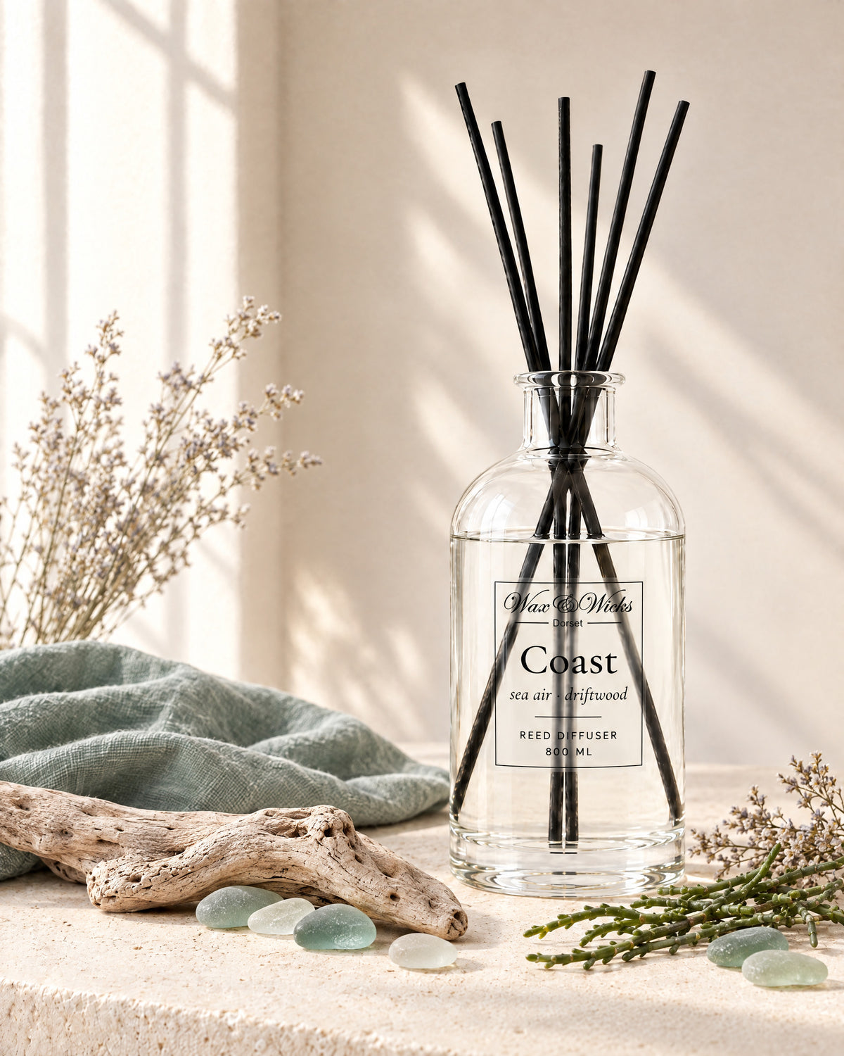 Coast 800 ml large reed diffuser in apothecary-style glass with extra-long reeds, styled with bleached driftwood, sea-glass pebbles, dried sea lavender and samphire