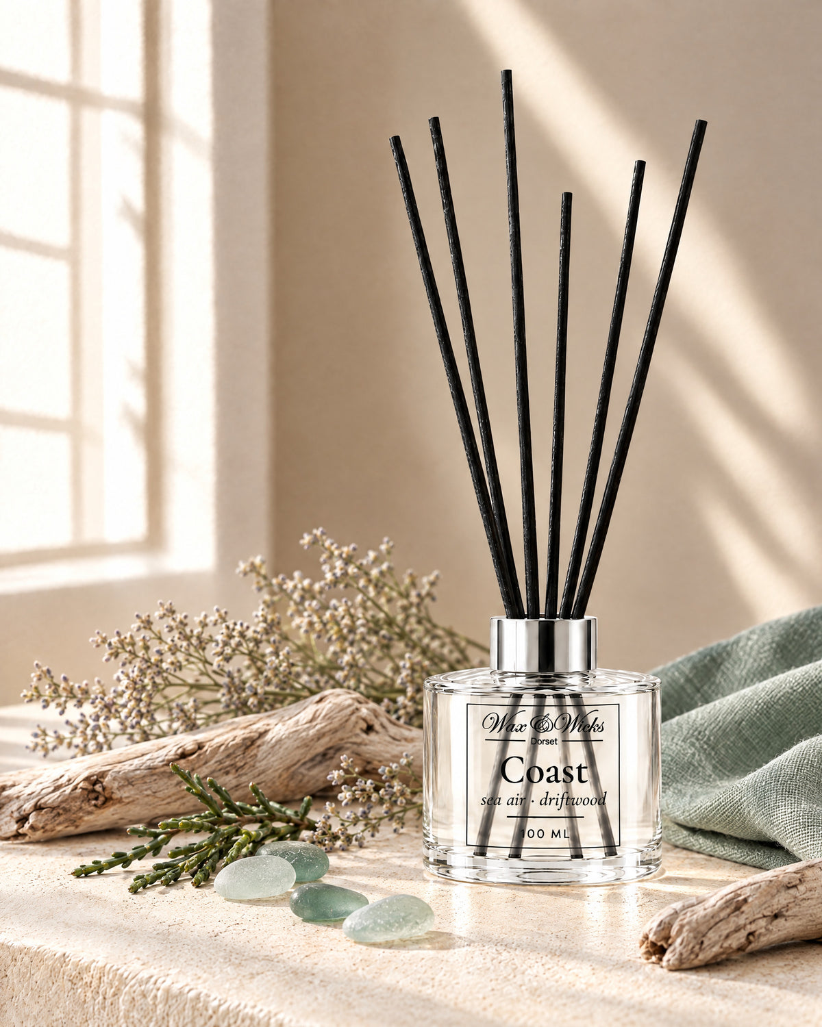 Coast 100 ml reed diffuser with black fibre reeds, styled with bleached driftwood, sea-glass pebbles, dried sea lavender and samphire