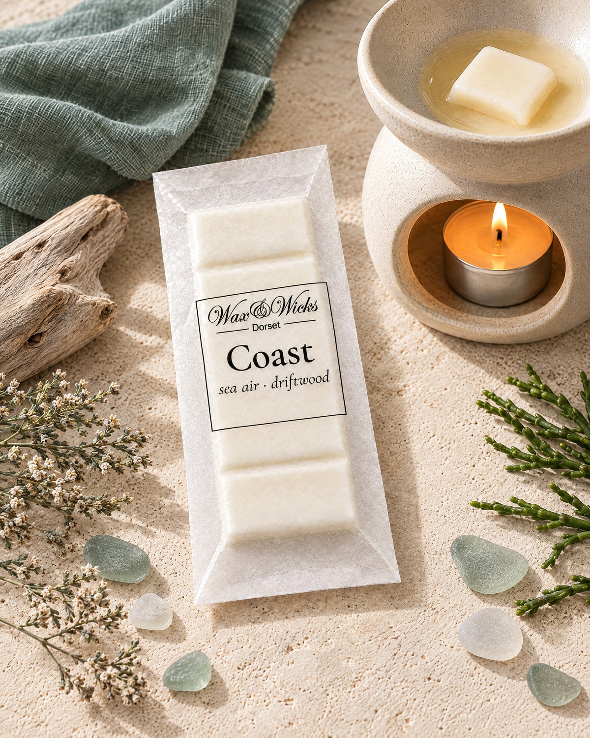 Coast wax melt snap bar, beside a tea-light wax burner, styled with bleached driftwood, sea-glass pebbles, dried sea lavender and samphire