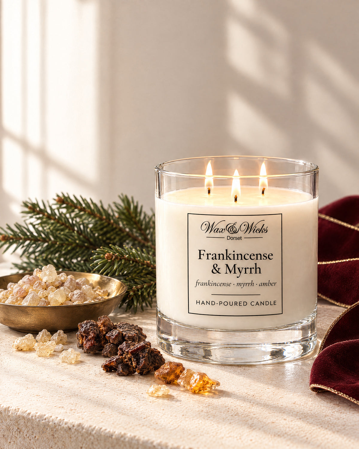 Large Frankincense & Myrrh candle, three wicks, in a clear glass jar, styled with frankincense and myrrh resin, a fir sprig and burgundy ribbon