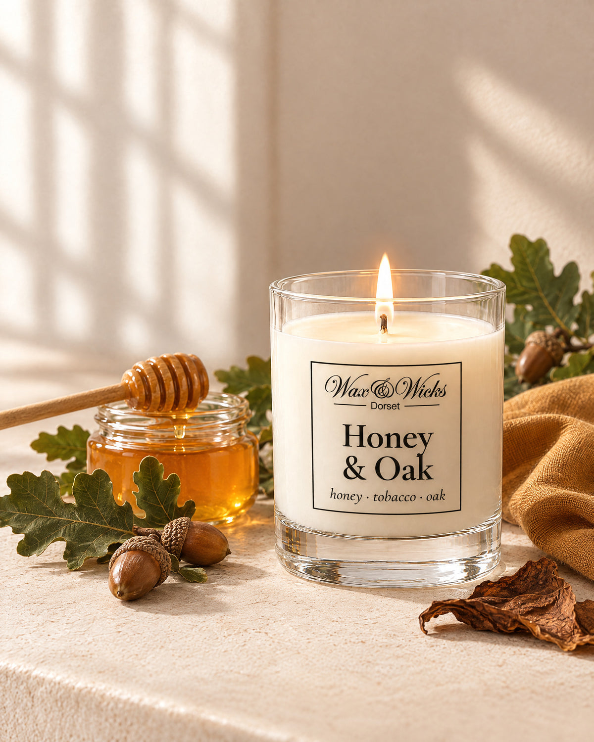 Small Honey & Oak candle, one wick, in a clear glass jar, styled with a jar of honey, oak leaves, acorns and tobacco leaf