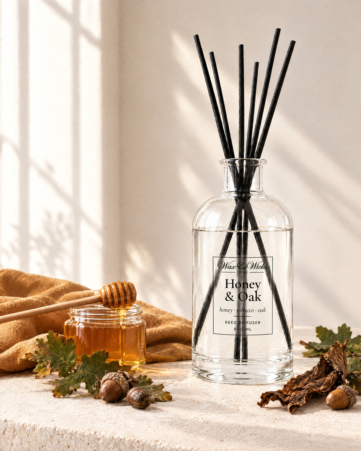 Honey & Oak 800 ml large reed diffuser in apothecary-style glass with extra-long reeds, styled with a jar of honey, oak leaves, acorns and tobacco leaf