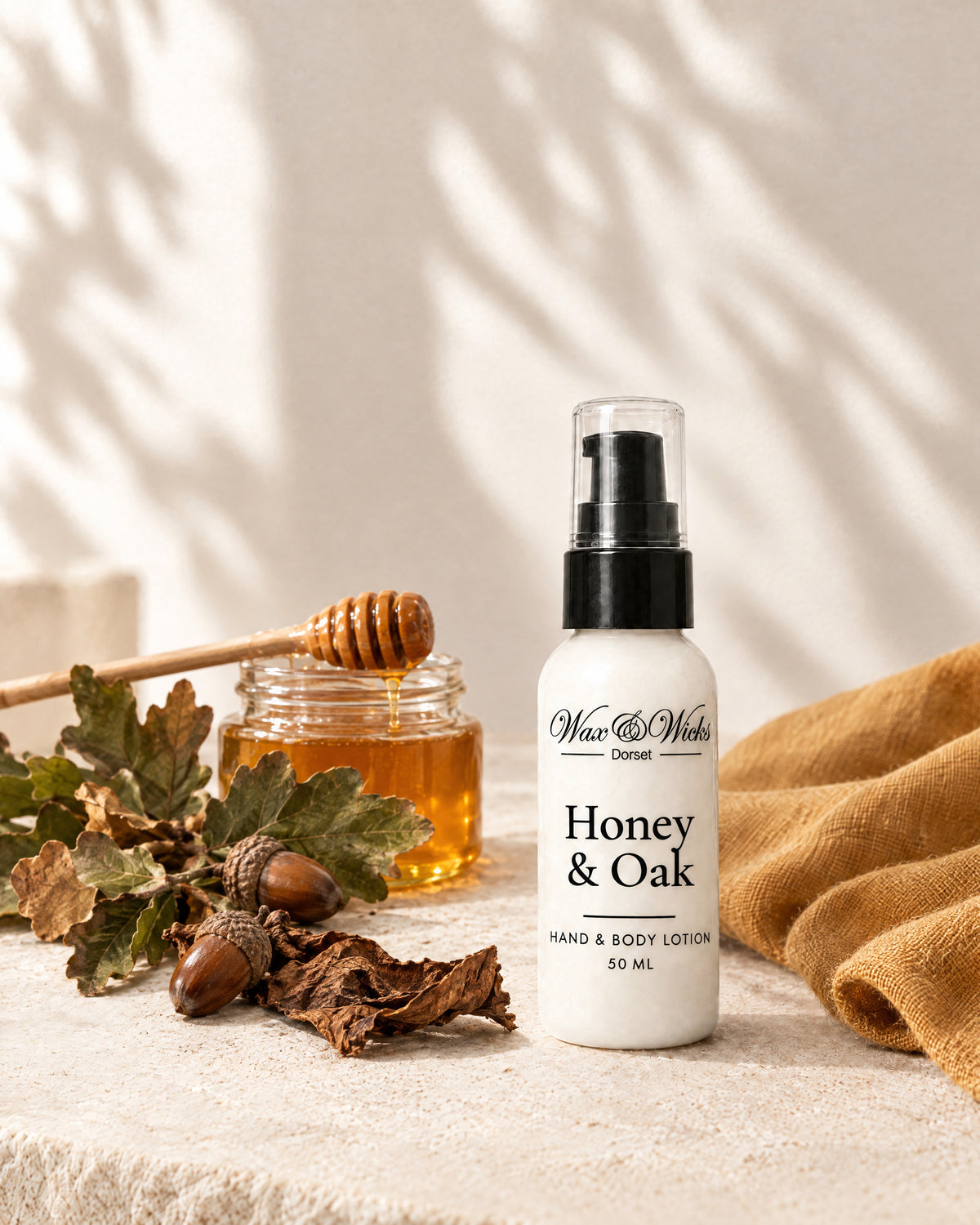 Honey & Oak hand & body lotion, 50 ml bottle, styled with a jar of honey, oak leaves, acorns and tobacco leaf