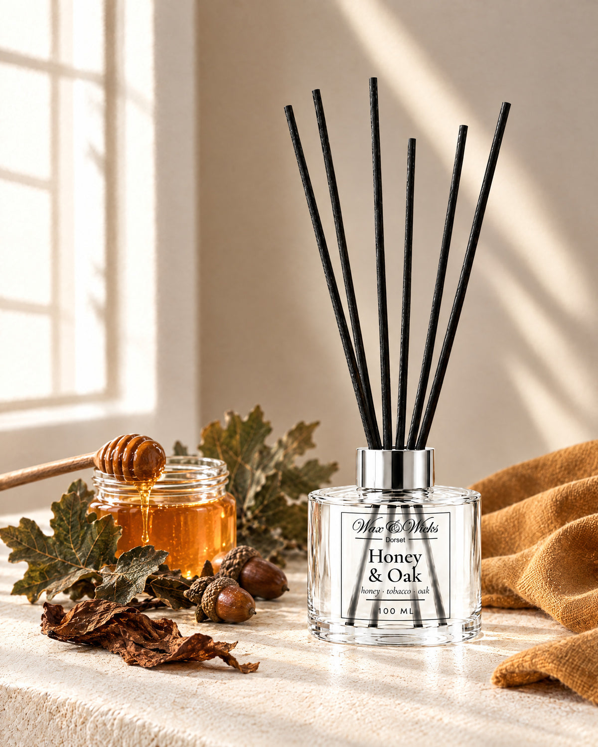 Honey & Oak 100 ml reed diffuser with black fibre reeds, styled with a jar of honey, oak leaves, acorns and tobacco leaf