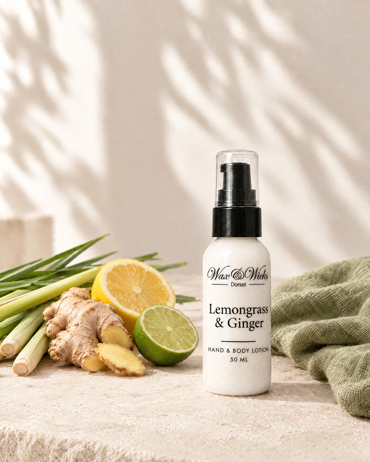 Lemongrass & Ginger hand & body lotion, 50 ml bottle, styled with lemongrass stalks, fresh ginger root, half a lemon and half a lime, with a sage-green linen
