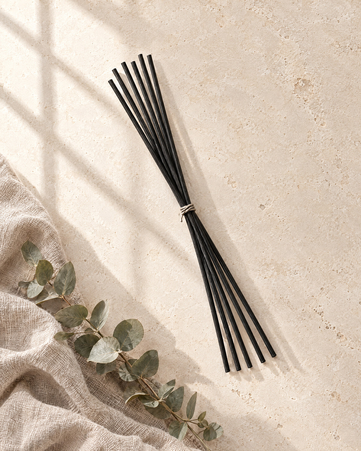 Black fibre replacement reeds tied with natural cord, lying on stone with linen and a sprig of eucalyptus