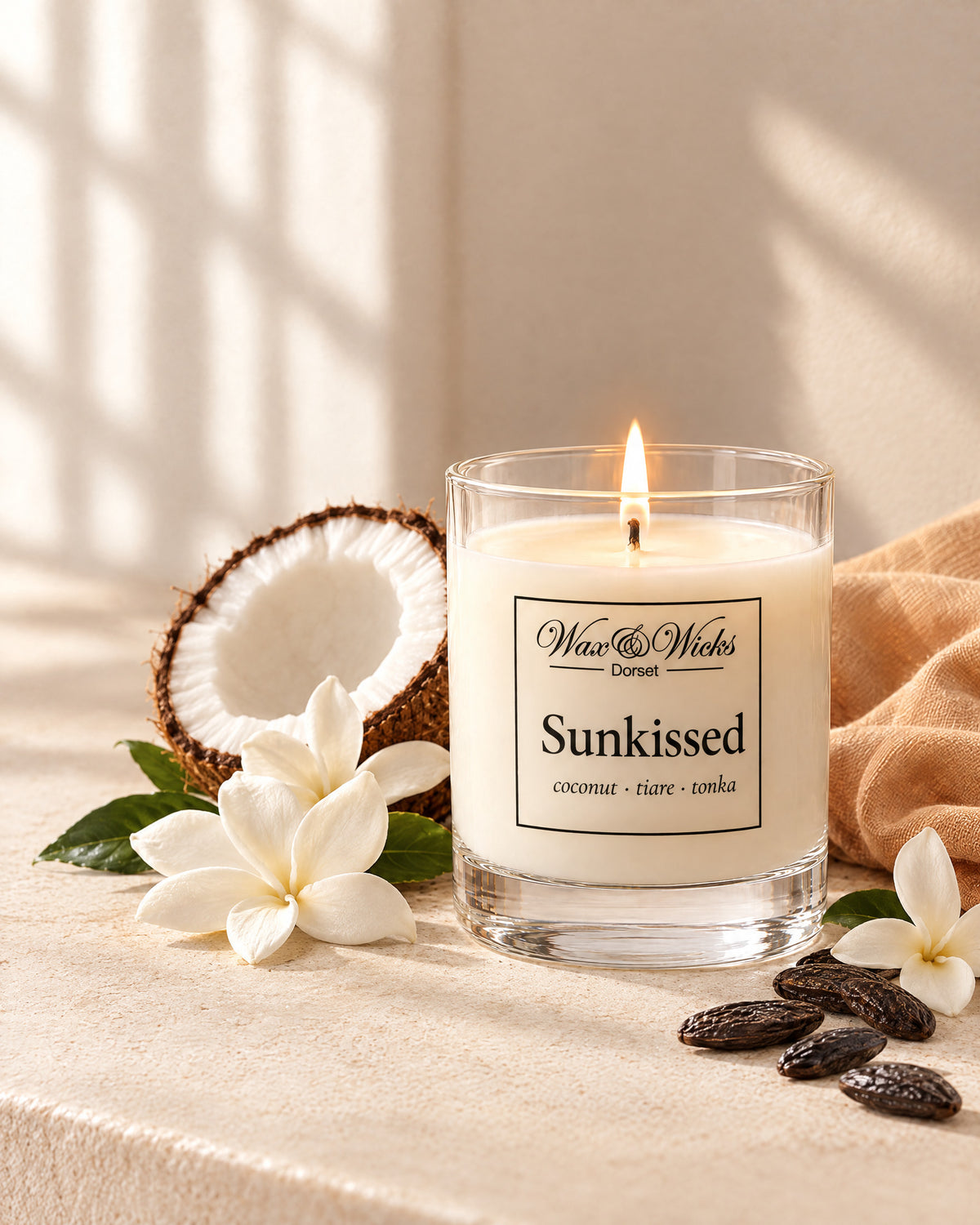 Small Sunkissed candle, one wick, in a clear glass jar, styled with half a coconut, white tiare flowers and tonka beans, with a peach linen