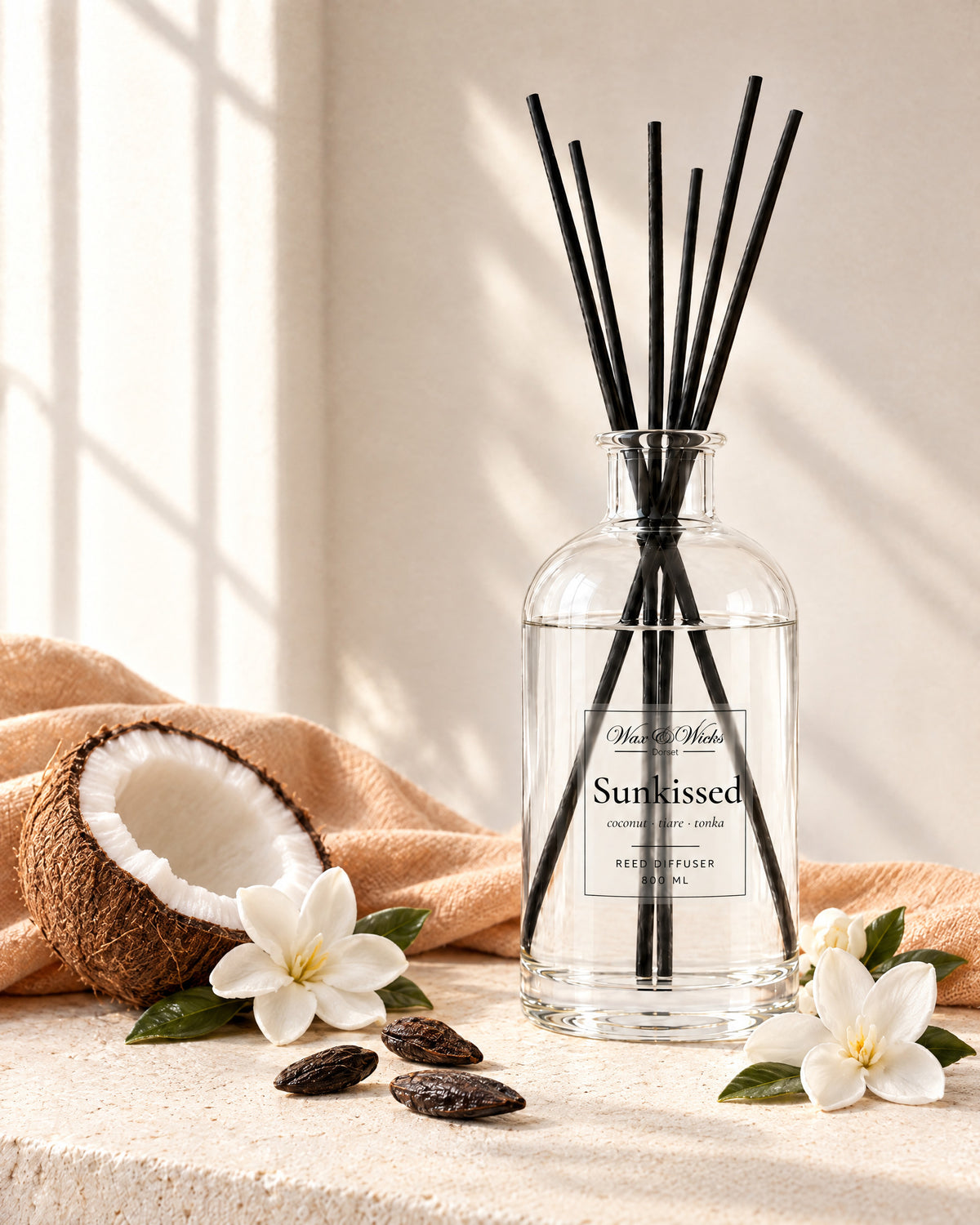 Sunkissed 800 ml large reed diffuser in apothecary-style glass with extra-long reeds, styled with half a coconut, white tiare flowers and tonka beans, with a peach linen