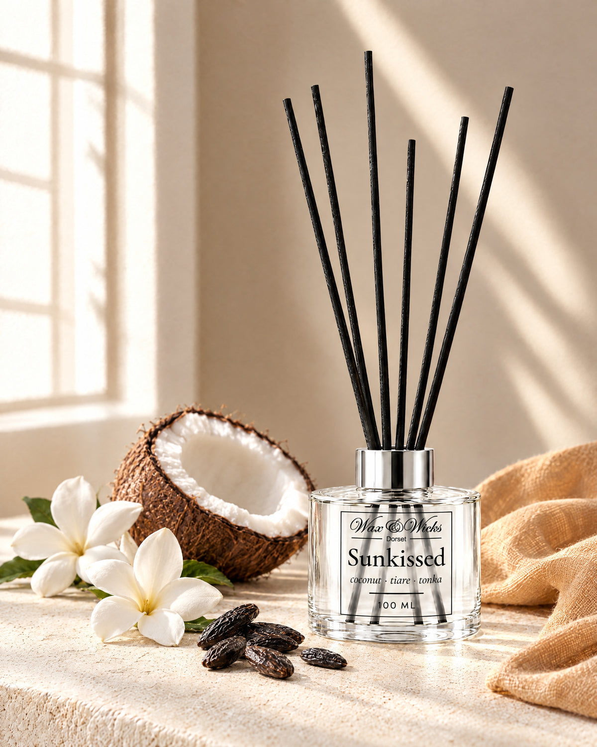 Sunkissed 100 ml reed diffuser with black fibre reeds, styled with half a coconut, white tiare flowers and tonka beans, with a peach linen
