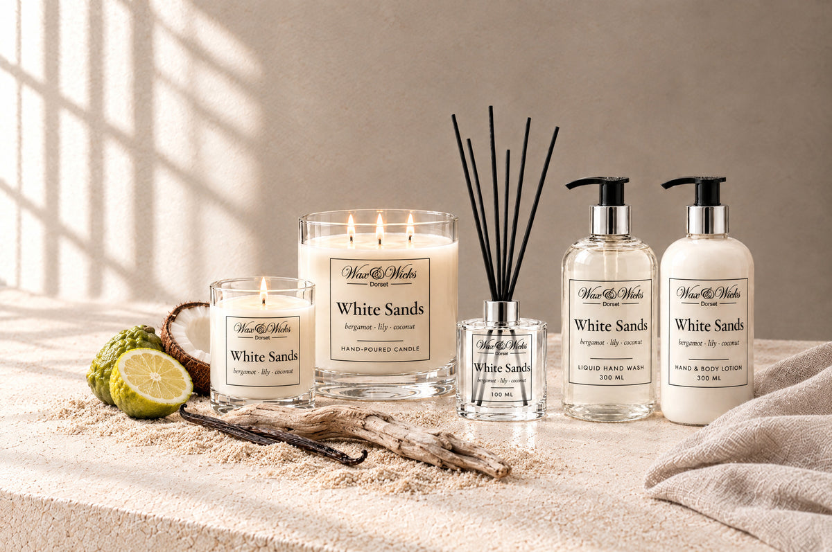 White Sands small and large candles, reed diffuser, hand wash and hand & body lotion together, styled with half a bergamot, half a coconut, a vanilla pod and driftwood on pale sand