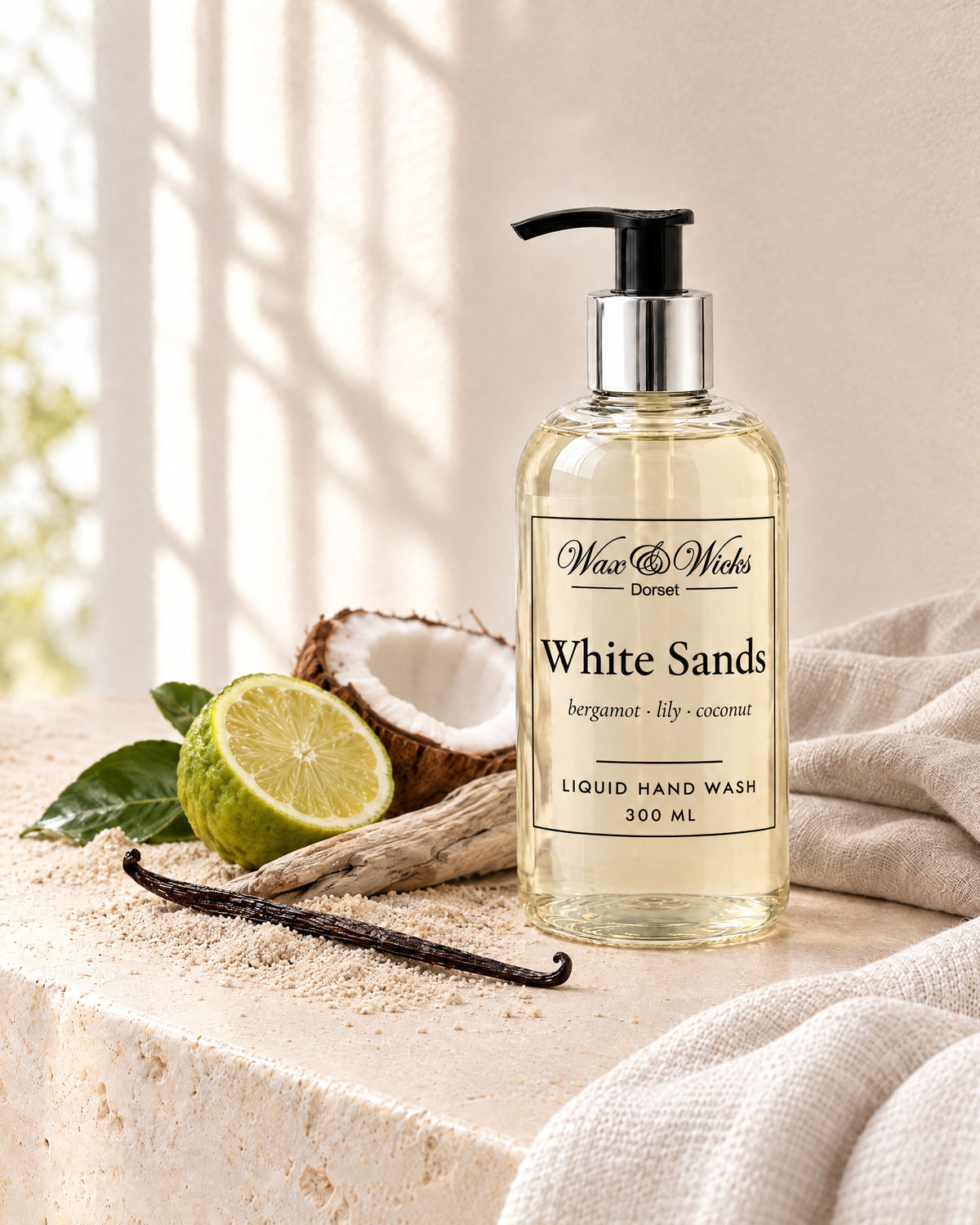 White Sands liquid hand wash, 300 ml pump bottle, styled with half a bergamot, half a coconut, a vanilla pod and driftwood on pale sand