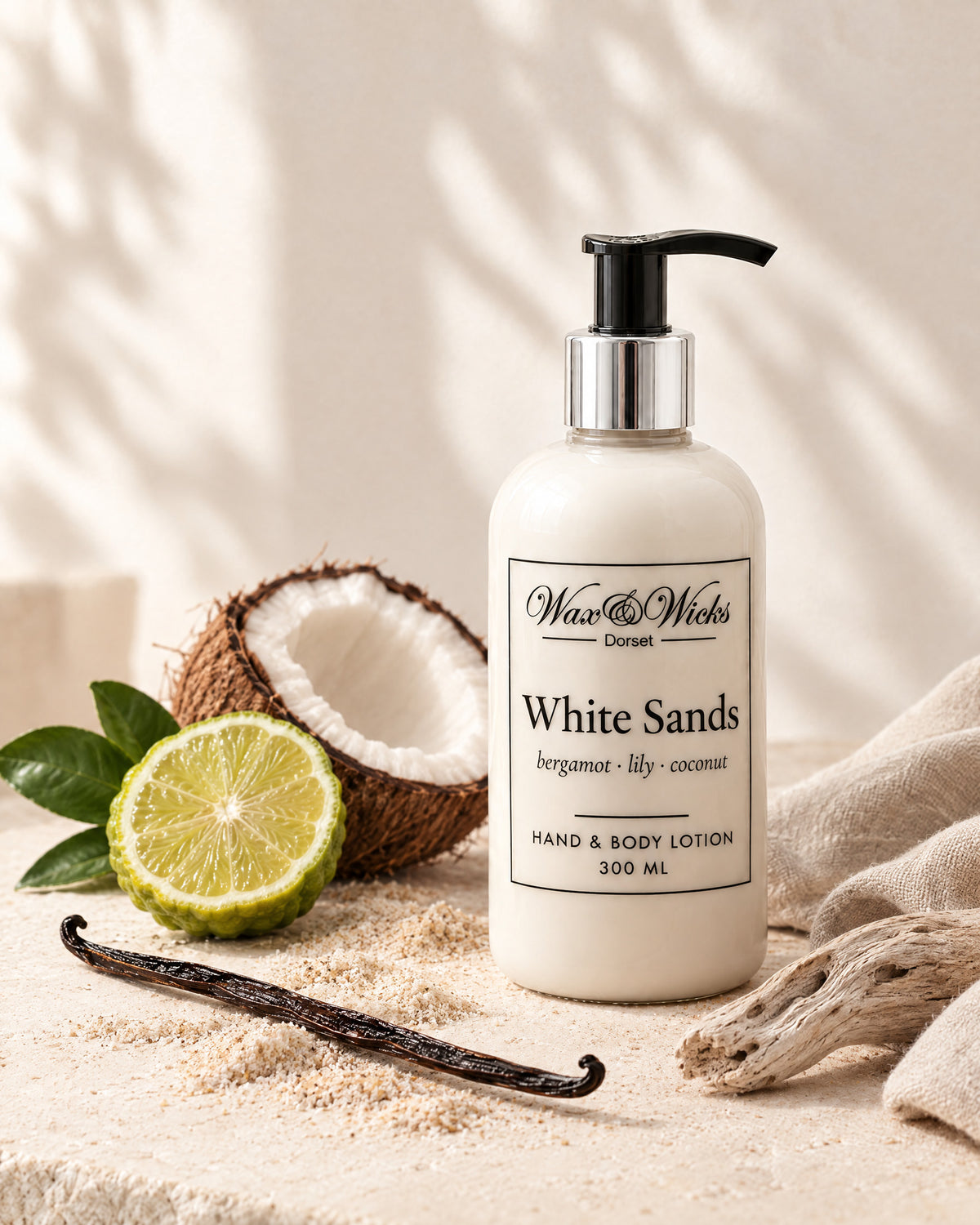 White Sands hand & body lotion, 300 ml pump bottle, styled with half a bergamot, half a coconut, a vanilla pod and driftwood on pale sand