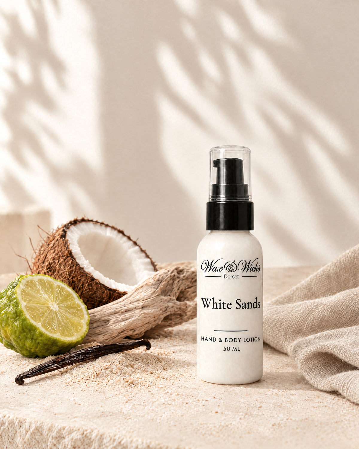 White Sands hand & body lotion, 50 ml bottle, styled with half a bergamot, half a coconut, a vanilla pod and driftwood on pale sand