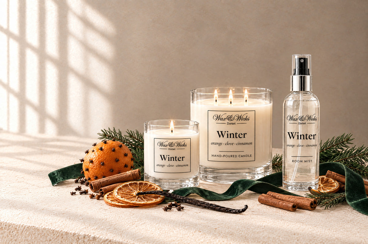 Winter candles and home fragrance together, styled with a clove-studded orange, dried orange slices, cinnamon sticks and fir